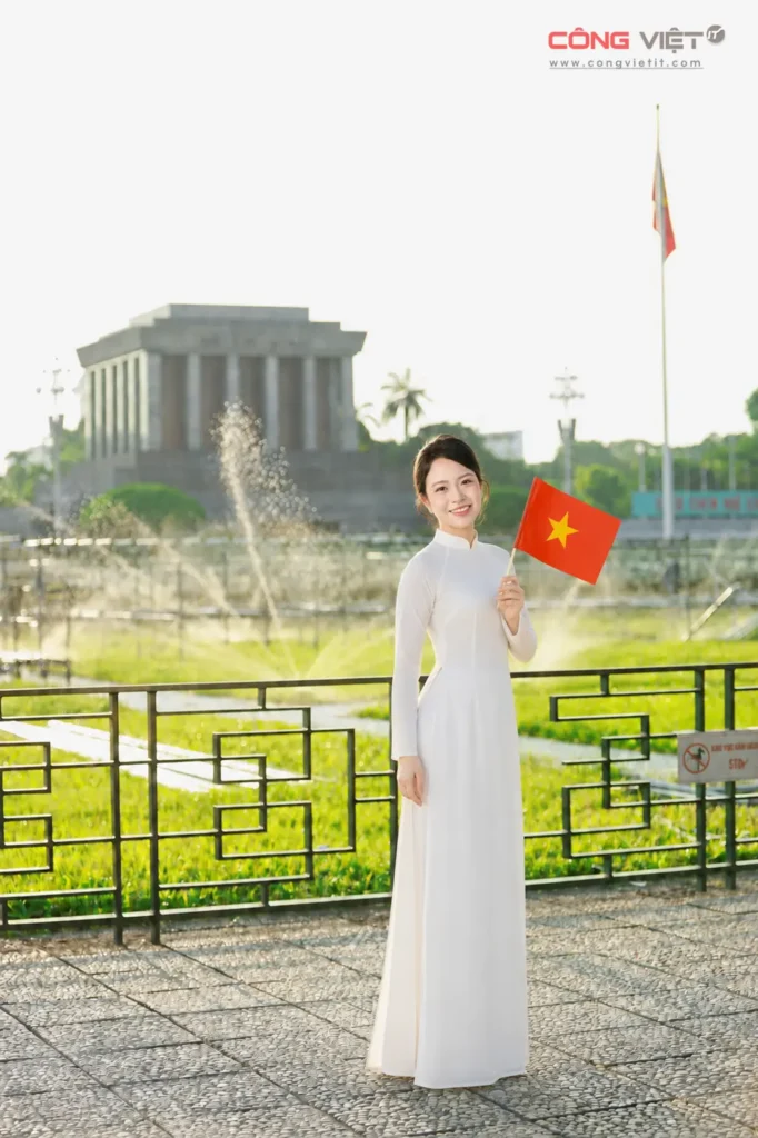 Người phụ nữ mặc áo dài trắng tạo dáng nghiêng với cờ đỏ sao vàng dịp 2/9